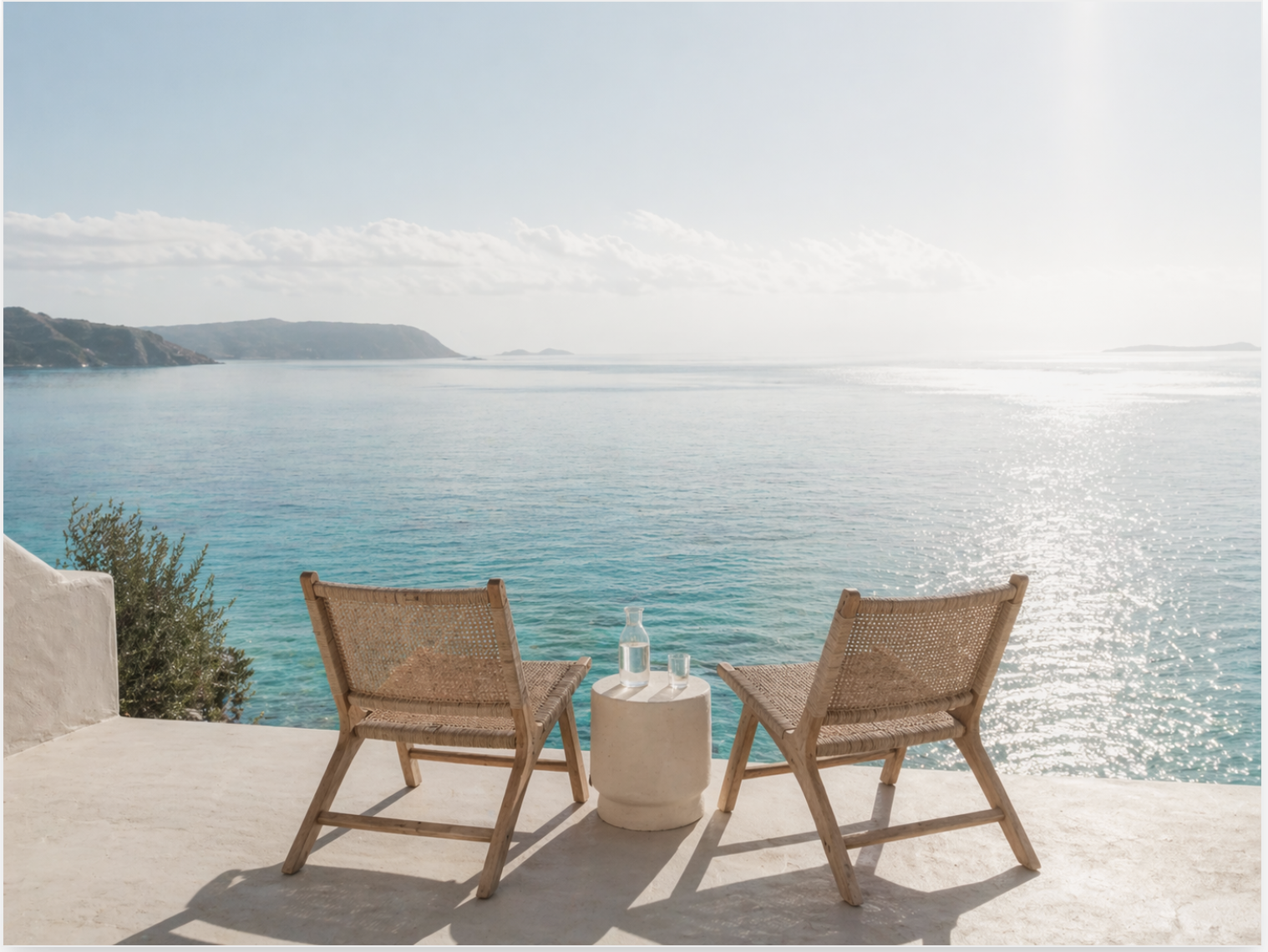 Two woven chairs on a terrace overlooking a calm turquoise sea